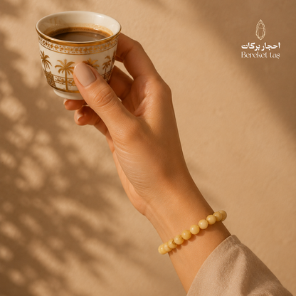 Amber stone bracelet with 8 mm yellow amber beads worn on the wrist, photographed with a coffee cup in warm natural light.