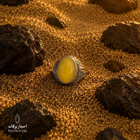 Yellow amber ring in 925 sterling silver, displayed on warm golden sand with natural stones.