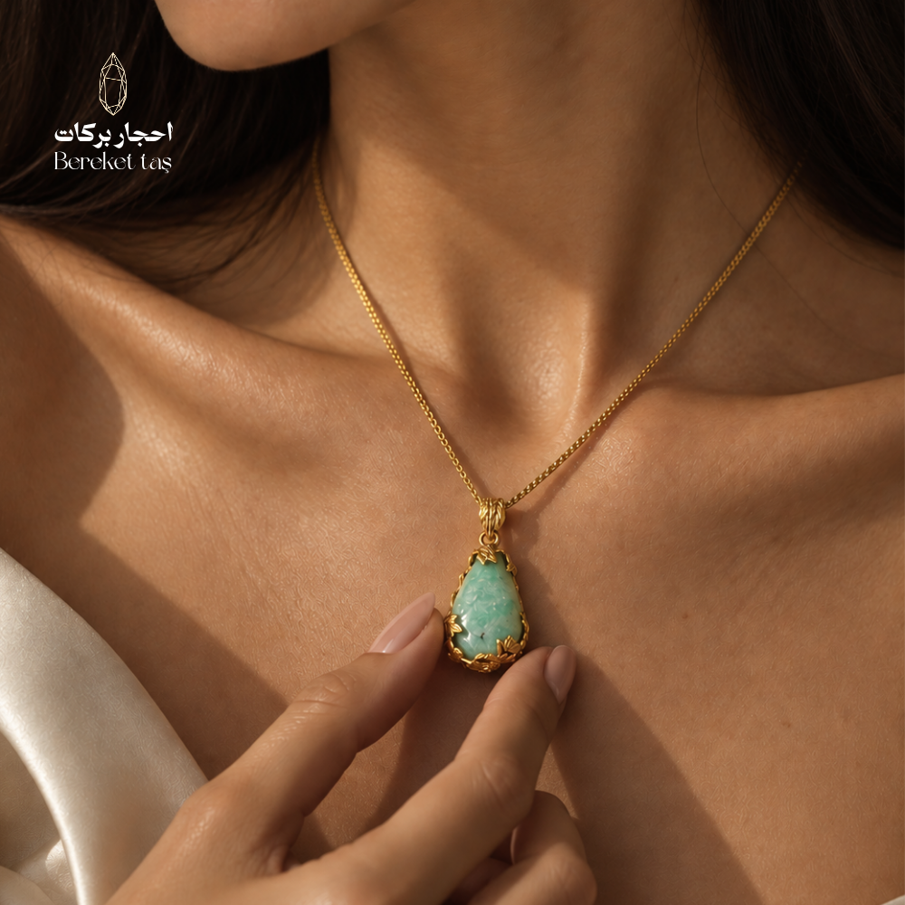 Close-up of a natural green Amazonite pendant necklace with a gold-plated chain worn against a white outfit