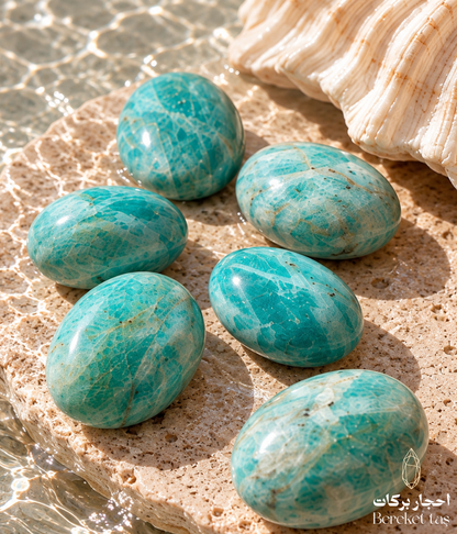 Collection of natural polished Amazonite stones in blue-green tones displayed on a warm stone surface beside clear water