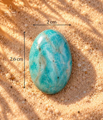 Natural polished Amazonite stone showing 2 cm width and 2.6 cm length on a sandy surface