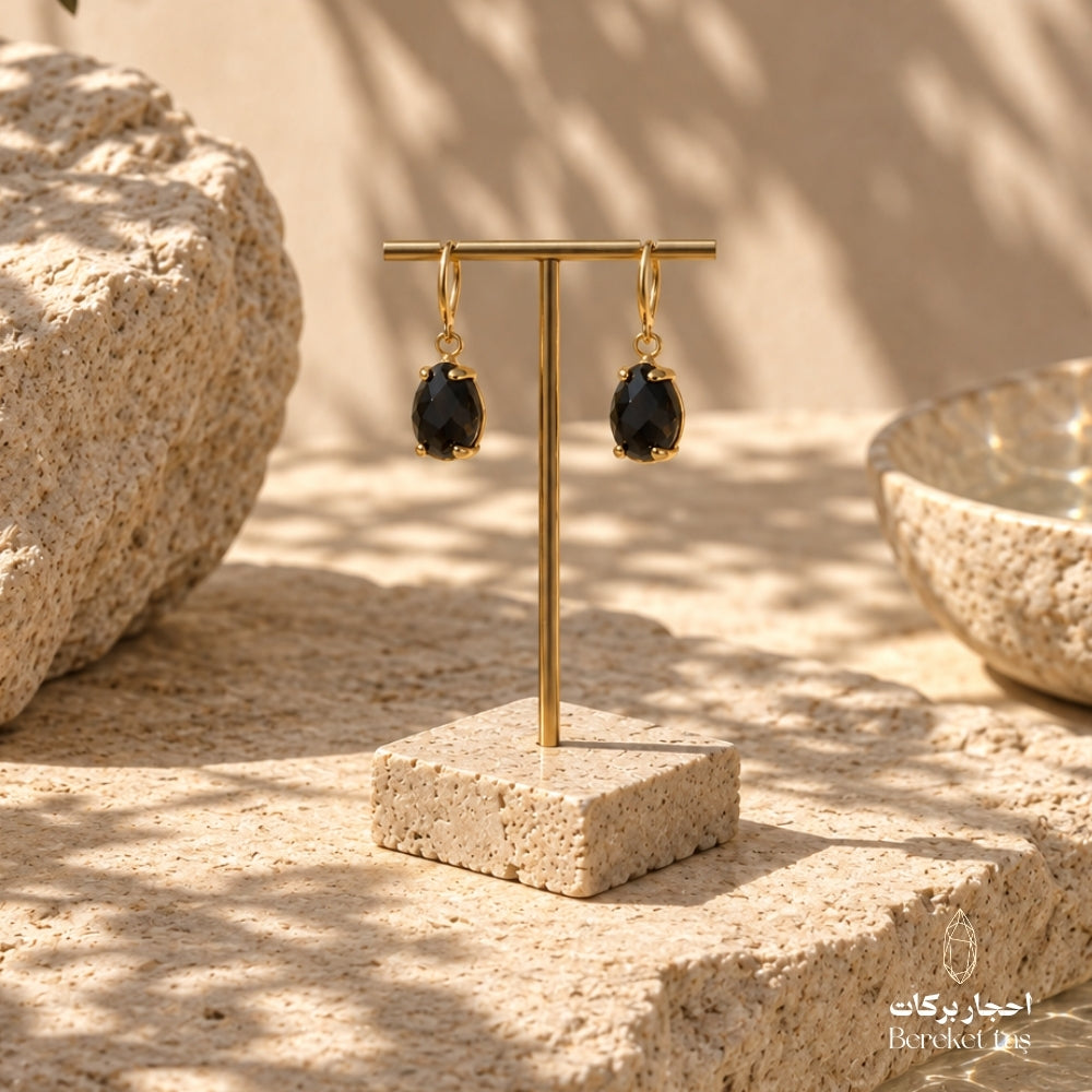 Natural Black Onyx drop earrings with gold-plated metal displayed on a stone jewelry stand