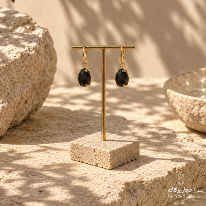 Natural Black Onyx drop earrings with gold-plated metal displayed on a stone jewelry stand