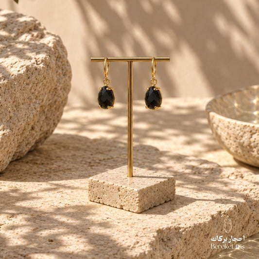 Natural Black Onyx drop earrings with gold-plated metal displayed on a stone jewelry stand