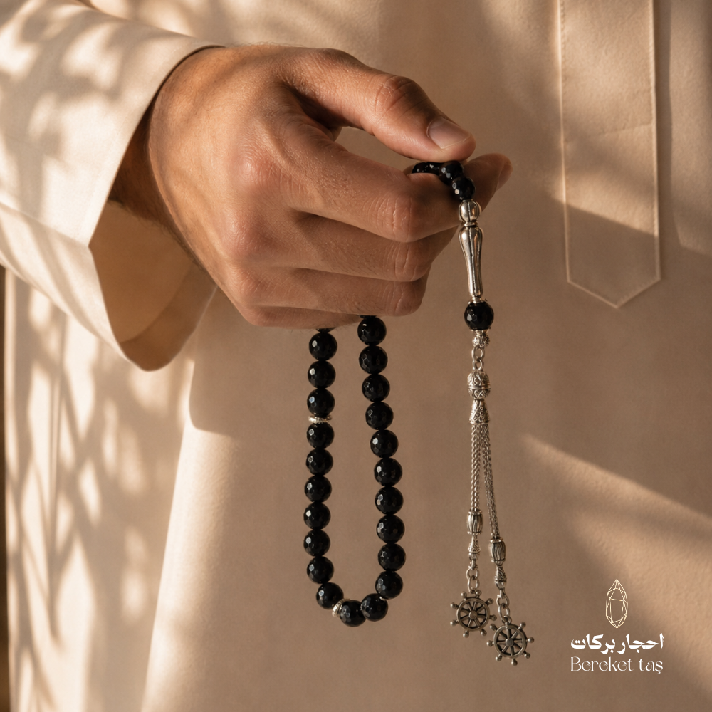 Natural black onyx tasbih with smooth 10 mm beads held in hand, featuring elegant metal details by Bereket Taş