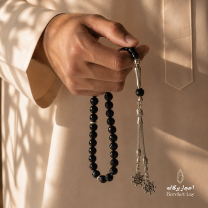 Natural black onyx tasbih with smooth 10 mm beads held in hand, featuring elegant metal details by Bereket Taş