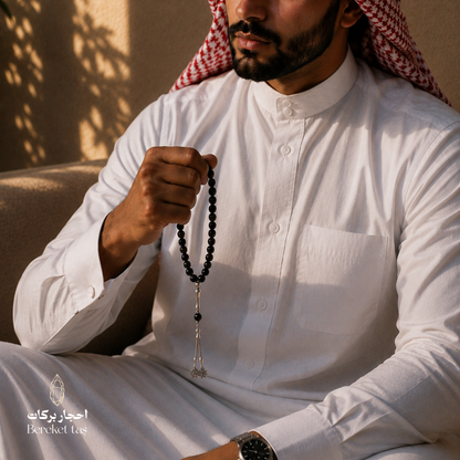 Man wearing a white thobe holding a natural black onyx tasbih by Bereket Taş