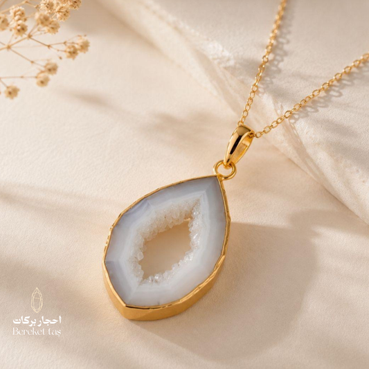 Natural Chalcedony pendant necklace with a gold-plated setting displayed on soft beige fabric