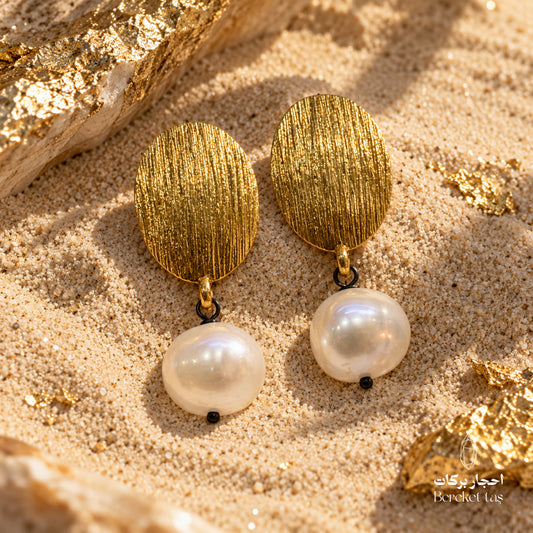 Handcrafted natural Pearl earrings with textured gold-plated metal, displayed on a sandy stone surface