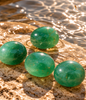 Natural polished green Fluorite stones displayed on a warm stone surface beside clear water