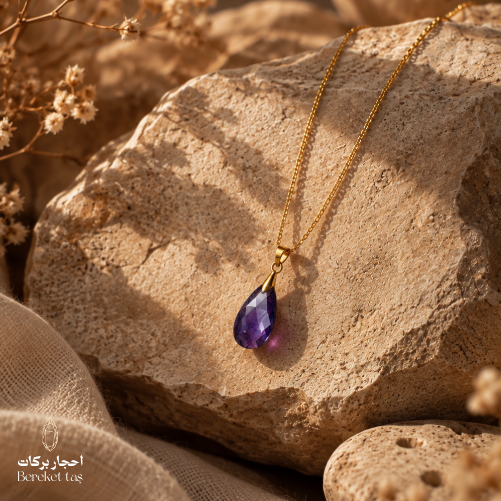Natural Amethyst pendant necklace with a gold-plated chain displayed on a warm textured stone surface