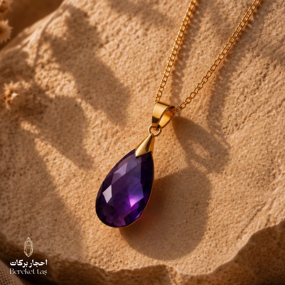 Natural Amethyst teardrop pendant necklace with a gold-plated chain displayed on a warm textured stone surface