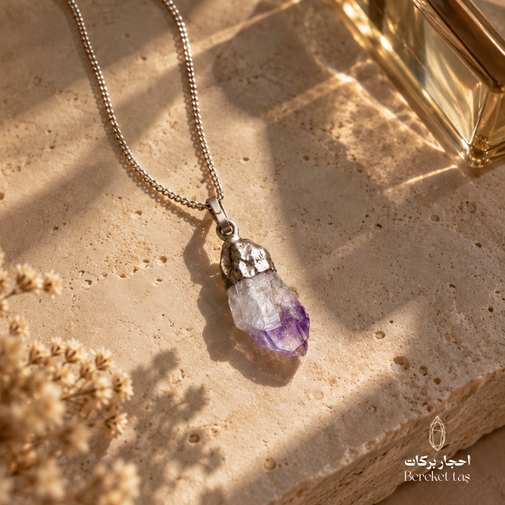 Natural Amethyst pendant necklace with a silver chain displayed on a warm beige stone surface