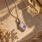 Natural Amethyst pendant necklace with a silver chain displayed on a warm beige stone surface