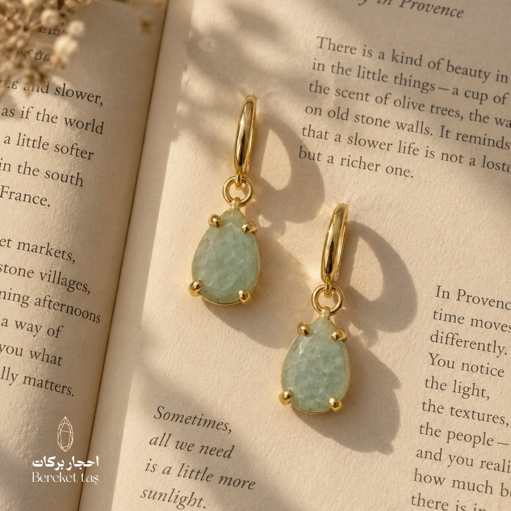 Natural Aquamarine teardrop earrings with gold-plated metal displayed on an open book