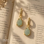 Natural Aquamarine teardrop earrings with gold-plated metal displayed on an open book