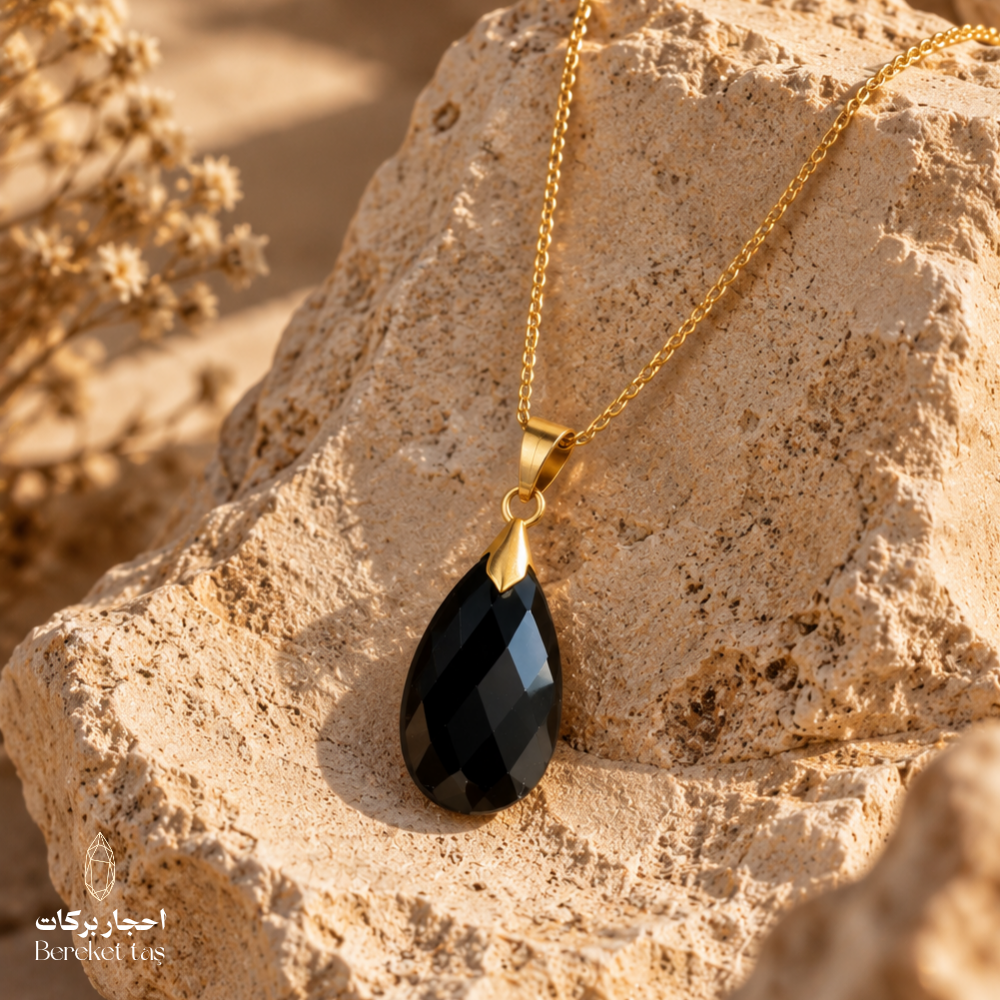 Natural Black Onyx teardrop pendant with a gold-plated chain displayed on a warm textured stone surface