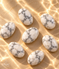 Natural polished Brazilian Howlite stones with white surfaces and gray and black veining arranged on a warm beige background