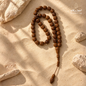 Natural Kuka Prayer Beads arranged on a sandy stone surface, showcasing polished brown wooden beads and classic design