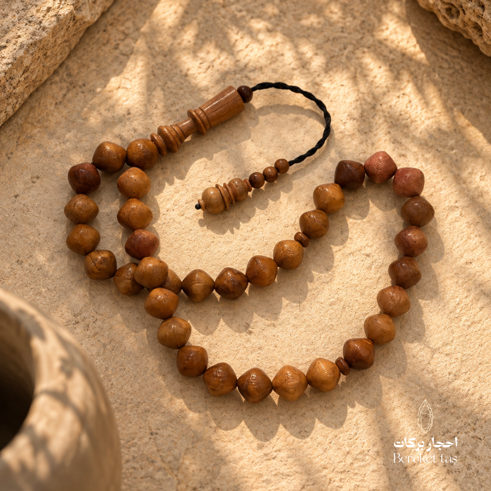 Natural Kuka Prayer Beads with polished brown beads in warm natural tones, displayed on a textured stone surface