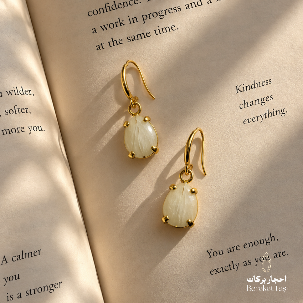 Natural Moonstone earrings with gold-plated metal displayed on an open book in warm natural light