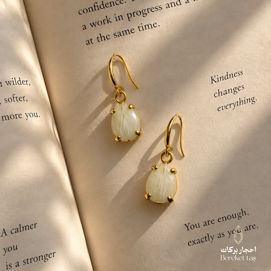 Natural Moonstone earrings with gold-plated metal displayed on an open book in warm natural light