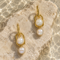 Natural Pearl earrings with gold-plated copper, elegantly displayed on a textured stone beside clear water