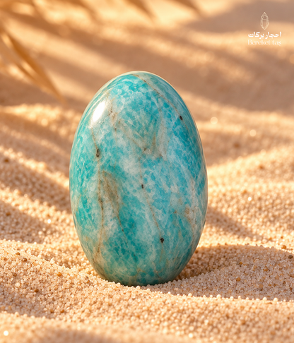Natural polished Amazonite stone with blue-green tones and natural veining displayed on warm sand