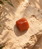 Natural polished red Carnelian stone displayed on a warm textured beige stone surface with soft sunlight