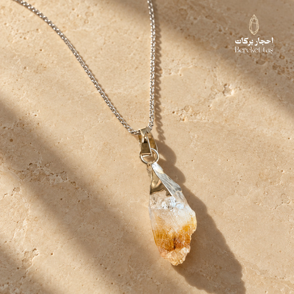 Natural raw Citrine pendant necklace with a silver chain displayed on a warm beige stone surface