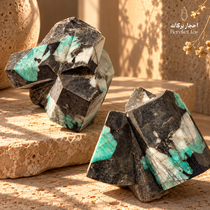 Natural raw Emerald stones with green and white mineral patterns displayed on a warm beige stone surface
