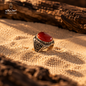 Natural Red Agate men's ring in 925 Sterling Silver displayed on warm desert sand, highlighting the polished red gemstone and ornate silver setting.