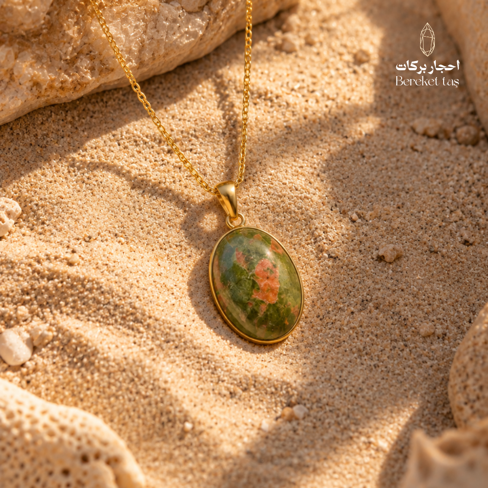 Natural Unakite pendant necklace with a gold-plated setting displayed on warm sand, showing green, orange, and brown stone tones