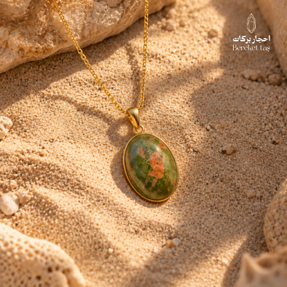 Natural Unakite pendant necklace with a gold-plated setting displayed on warm sand, showing green, orange, and brown stone tones