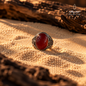 Natural Red Agate ring in 925 Sterling Silver displayed on warm sand, highlighting the polished red gemstone and ornate silver setting.