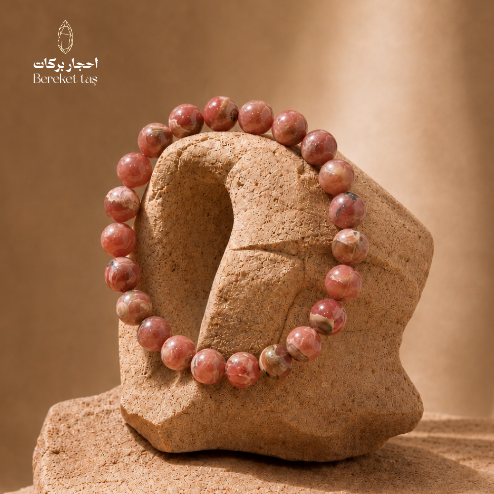 Pink Rhodochrosite stone bracelet with 8 mm beads displayed on a natural stone sculpture
