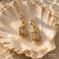 Natural Rutilated Quartz earrings with gold-plated metal displayed on a seashell