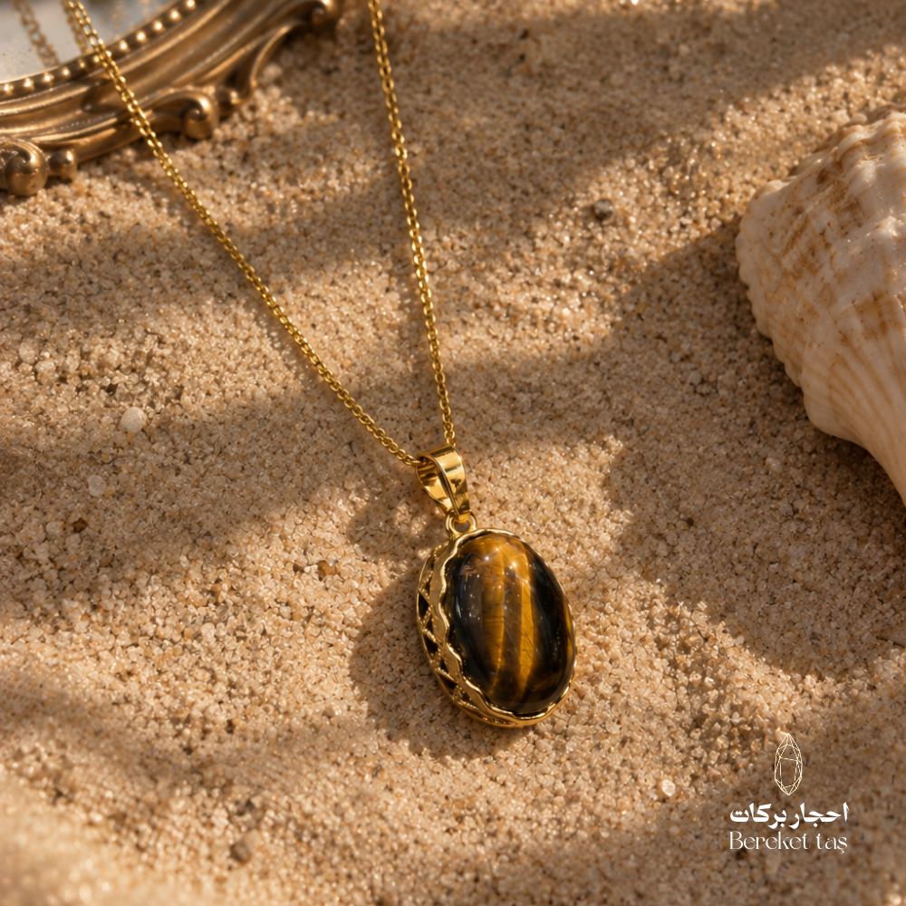 Natural Tiger Eye pendant necklace with a gold-plated chain displayed on warm sand